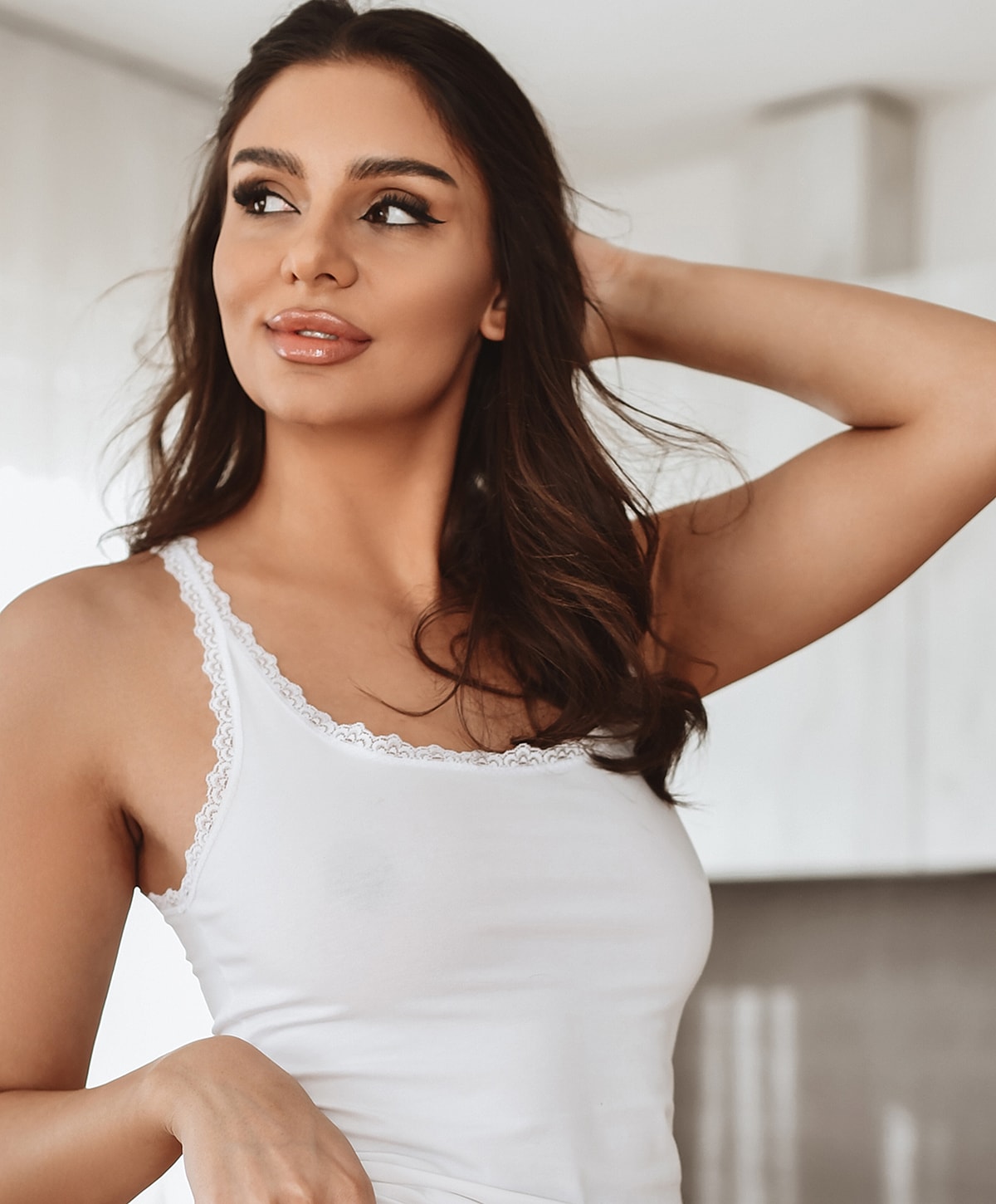 Woman in white tank top, looking thoughtfully.