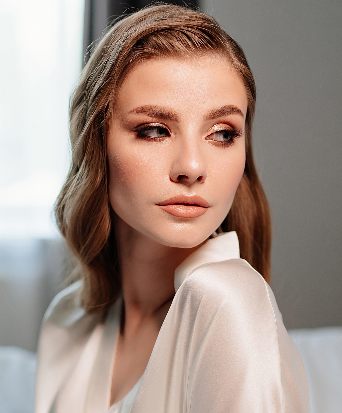 Elegant woman in soft light with subtle makeup.