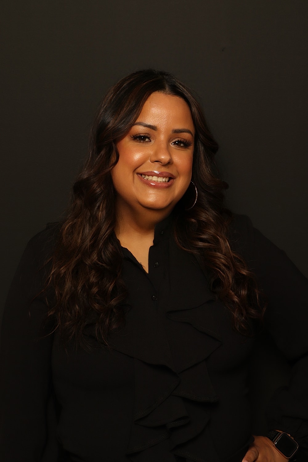 Smiling woman in a black blouse, dark background.