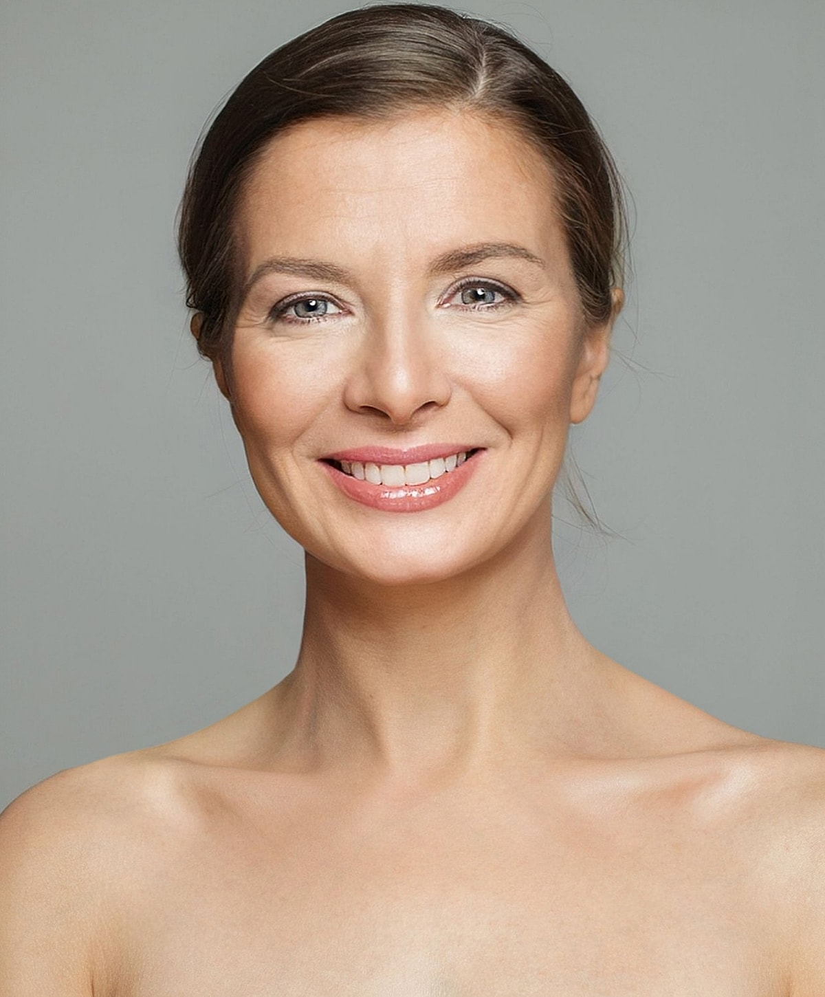 Smiling woman with natural makeup and neutral background.