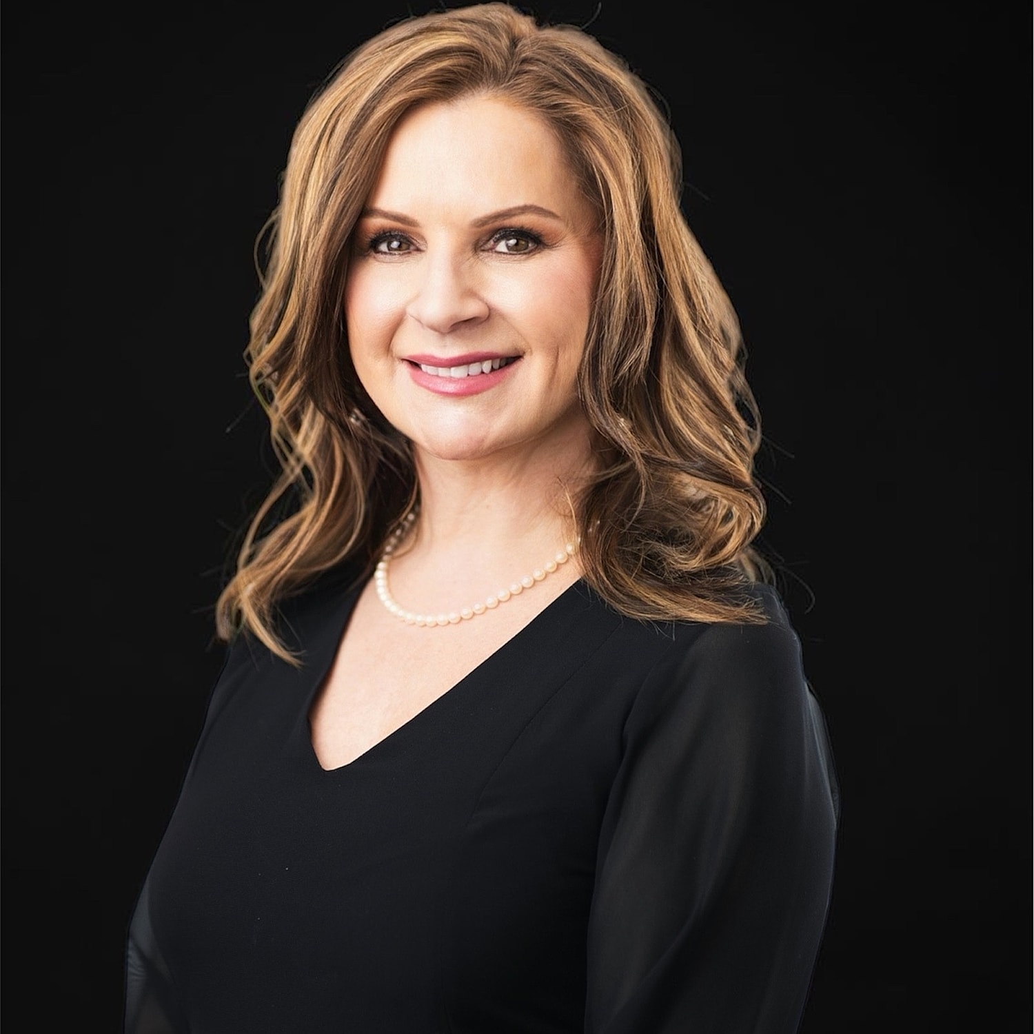 Smiling woman in black dress with pearl necklace.
