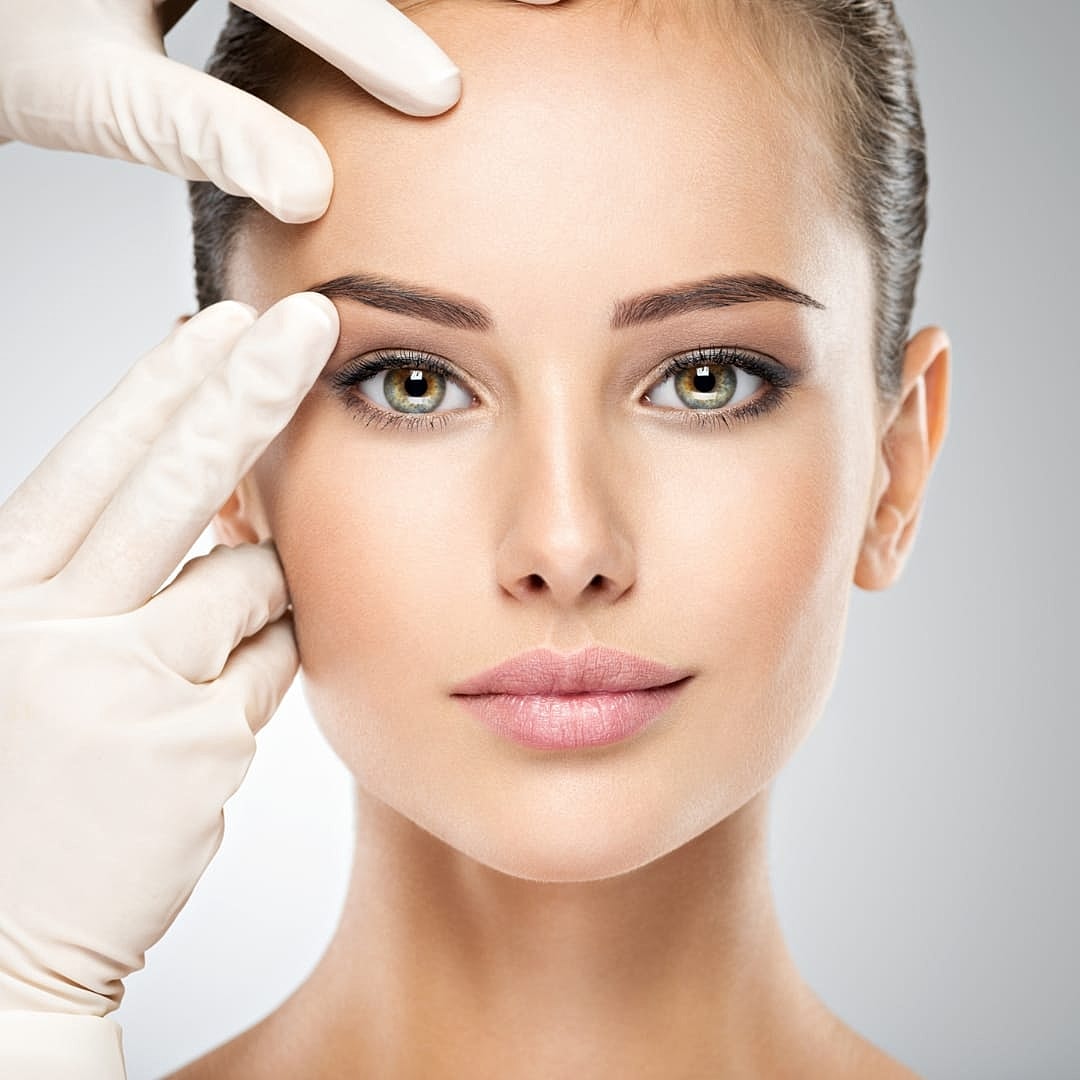 Woman receiving facial treatment with gloved hands.