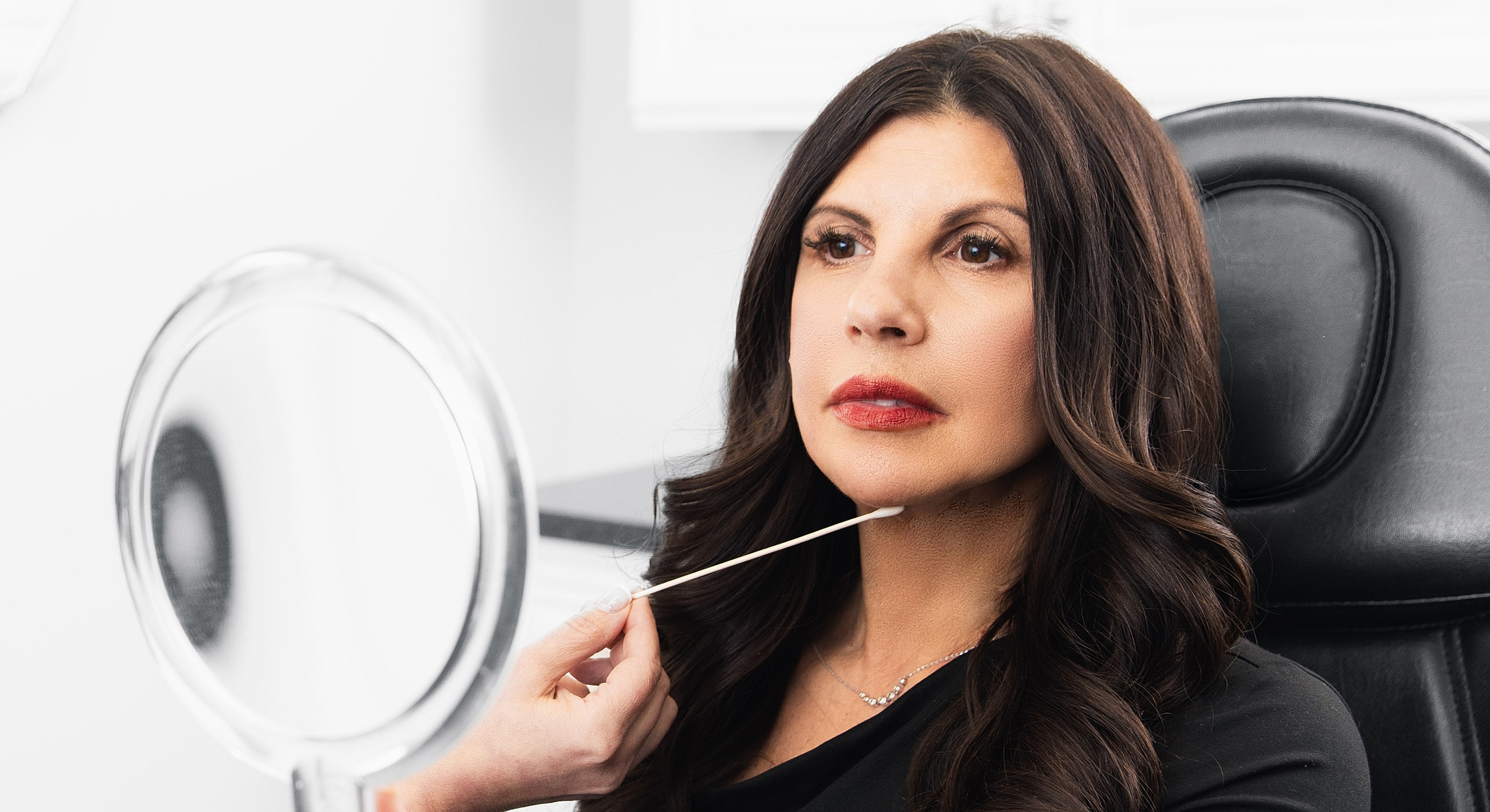 Woman applying skincare while looking in mirror.