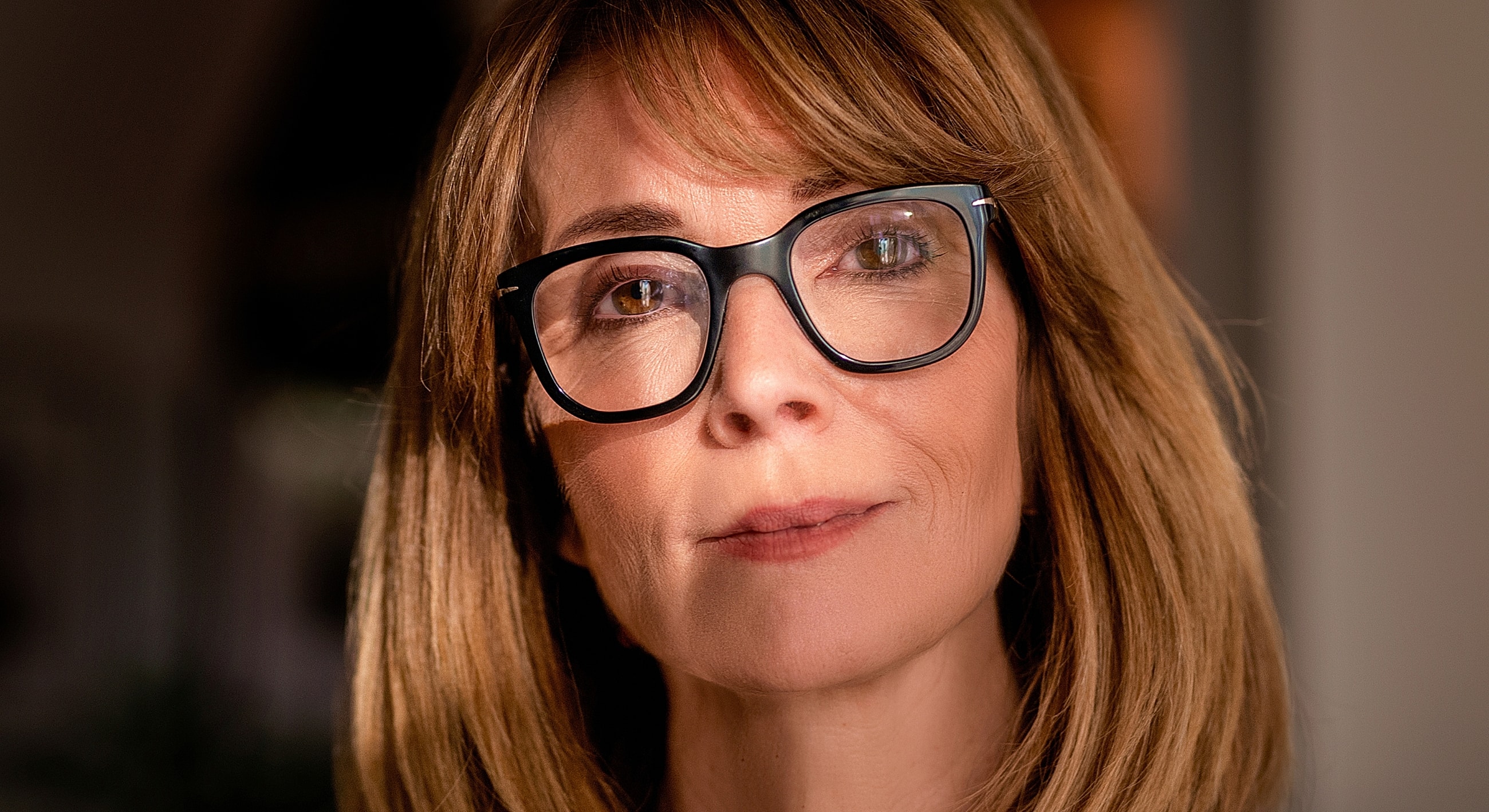 Woman with glasses, soft lighting, thoughtful expression.