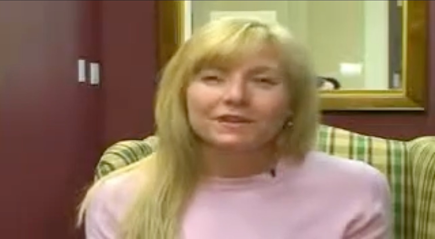 Woman in a pink sweater, sitting indoors.